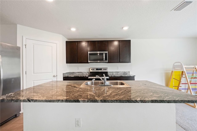 kitchen featuring stainless steel appliances, a sink, visible vents, a kitchen island with sink, and dark brown cabinets