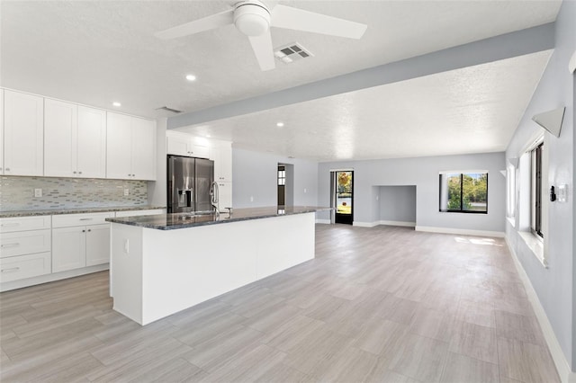 7049 Peninsular Dr, New Port Richey, FL 34652 - kitchen with stainless steel fridge, a center island with sink, dark stone countertops, white cabinets, and a ceiling fan