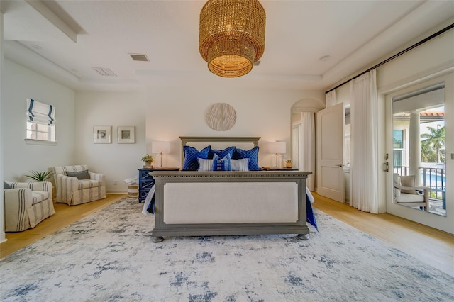 362 41st Ave, St Pete Beach, FL 33706 - bedroom with visible vents, light wood finished floors, access to exterior, a tray ceiling, and an inviting chandelier