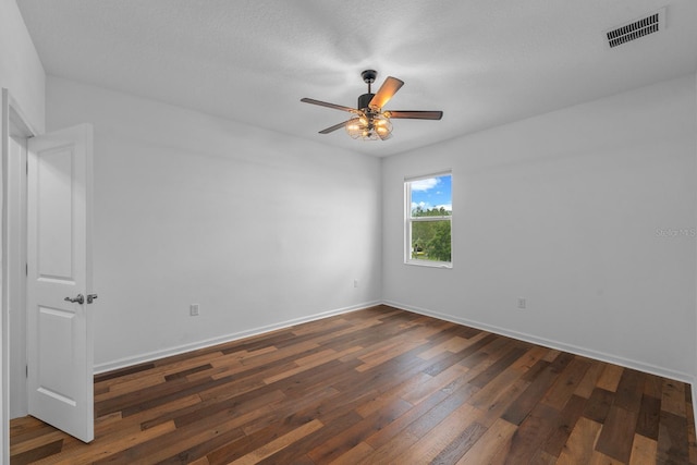 empty room with dark wood finished floors, visible vents, a ceiling fan, and baseboards