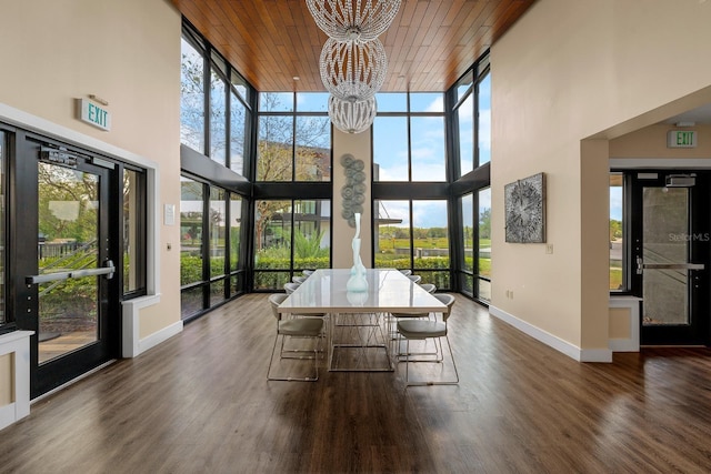 sunroom featuring baseboards, a high ceiling, a wealth of natural light, and a notable chandelier