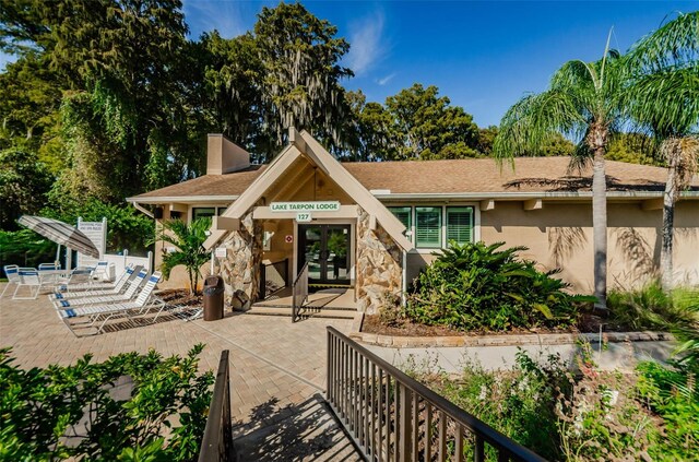 3143 Mission Grove Dr, Palm Harbor, FL 34684 - exterior space with a patio area, stone siding, a chimney, stucco siding, and french doors