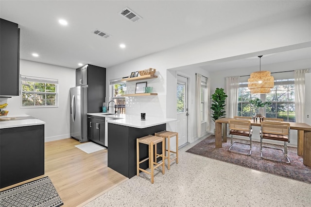 kitchen with light countertops, stainless steel fridge with ice dispenser, a breakfast bar, a sink, and visible vents