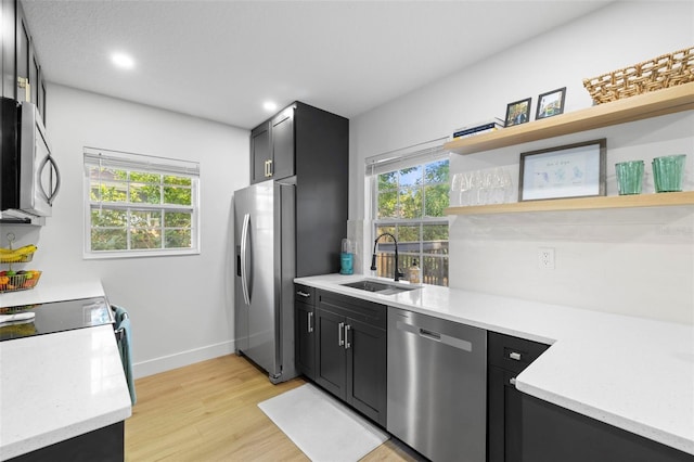 kitchen with light countertops, appliances with stainless steel finishes, a sink, open shelves, and dark cabinets