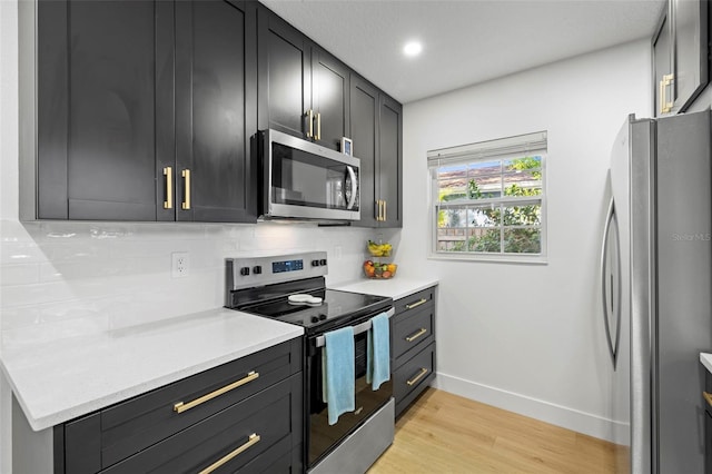 kitchen featuring decorative backsplash, light countertops, light wood finished floors, baseboards, and stainless steel appliances