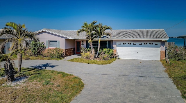 ranch-style home with a tile roof, stucco siding, driveway, brick siding, and a garage