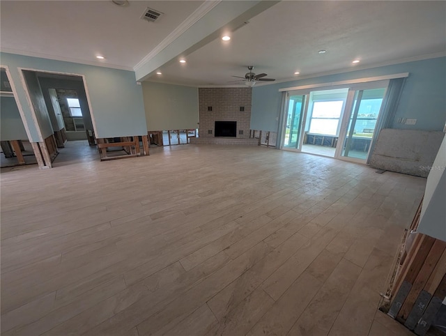 unfurnished living room featuring a ceiling fan, a fireplace, wood finished floors, visible vents, and ornamental molding