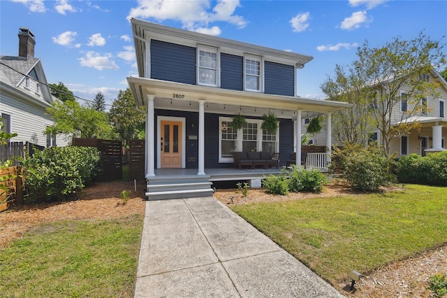 american foursquare style home featuring french doors, a front yard, a porch, and fence