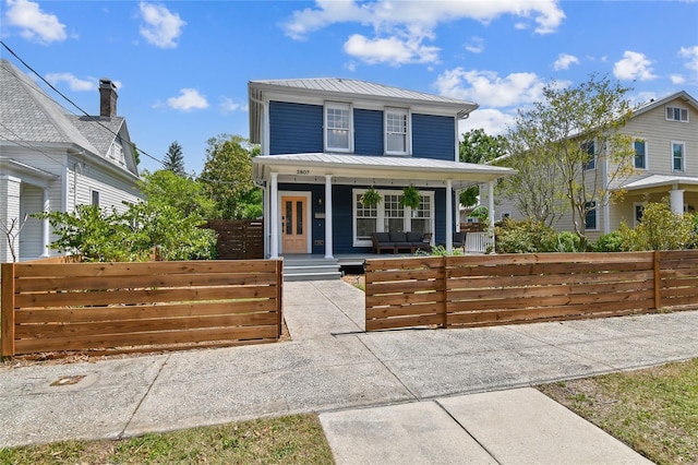 american foursquare style home featuring metal roof, a fenced front yard, and a porch