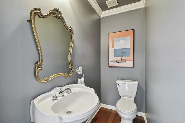 half bathroom with a sink, wood finished floors, baseboards, visible vents, and ornamental molding