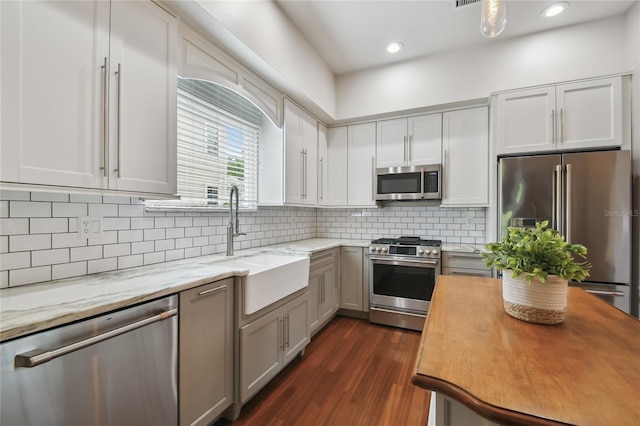 kitchen featuring tasteful backsplash, dark wood-style flooring, stainless steel appliances, a sink, and light stone counters