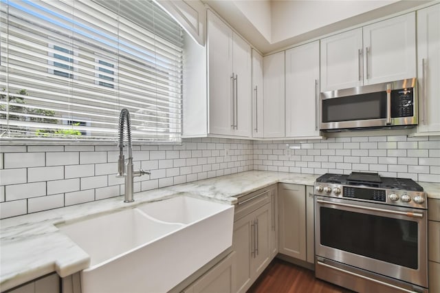kitchen featuring decorative backsplash, appliances with stainless steel finishes, white cabinetry, a sink, and light stone counters