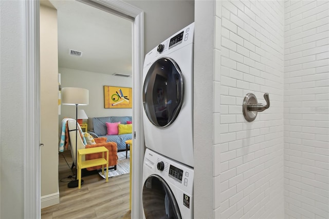 laundry room with visible vents, stacked washer / drying machine, laundry area, and wood finished floors