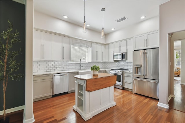 kitchen with light countertops, wood finished floors, high end appliances, decorative light fixtures, and backsplash
