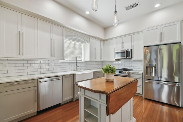 kitchen featuring dark wood-style flooring, visible vents, a sink, high quality appliances, and a center island