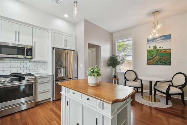 kitchen with backsplash, wood finished floors, appliances with stainless steel finishes, hanging light fixtures, and baseboards