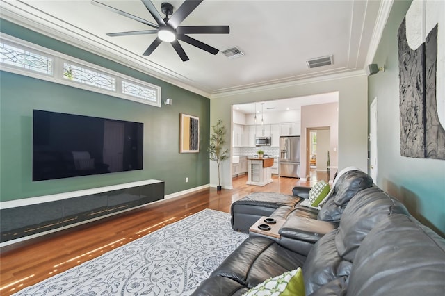 living room featuring light wood finished floors, visible vents, crown molding, and ceiling fan
