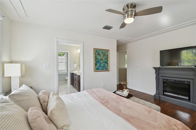 bedroom with visible vents, connected bathroom, baseboards, and wood finished floors