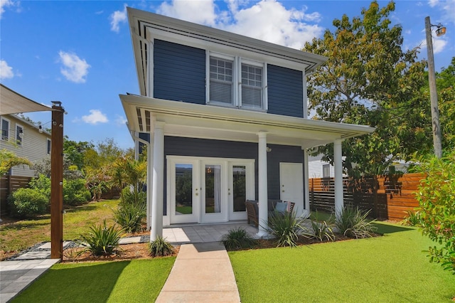 view of front of house featuring covered porch, fence, a front lawn, and french doors