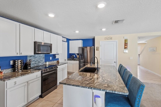 kitchen with light tile patterned flooring, a sink, appliances with stainless steel finishes, visible vents, and dark stone counters