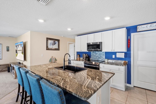 kitchen with white cabinets, a sink, appliances with stainless steel finishes, and dark stone countertops