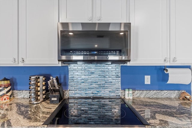 interior details with dark stone countertops, white cabinetry, stainless steel microwave, and cooktop