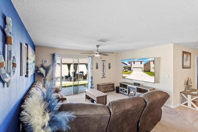 living area featuring baseboards, a textured ceiling, visible vents, a ceiling fan, and light carpet