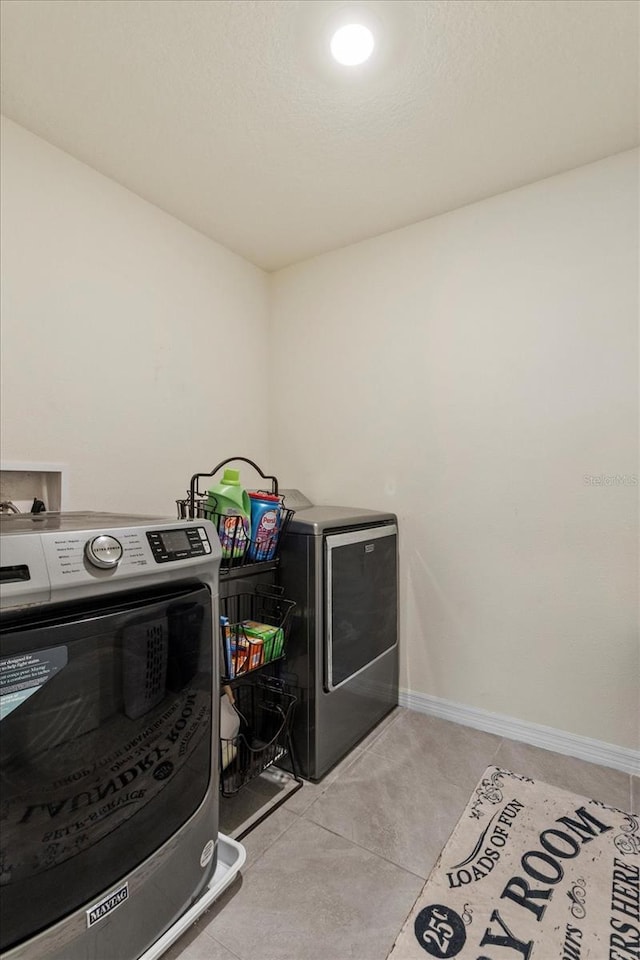 washroom with baseboards, light tile patterned floors, laundry area, and washer and clothes dryer