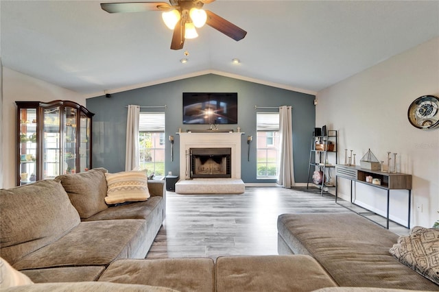 living room with ceiling fan, a fireplace with raised hearth, wood finished floors, lofted ceiling, and baseboards