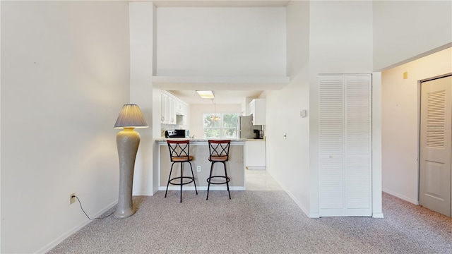 kitchen featuring white cabinets, a kitchen breakfast bar, a peninsula, light carpet, and light countertops