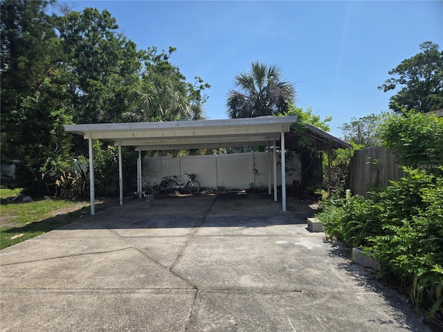 view of parking with driveway, a detached carport, and fence