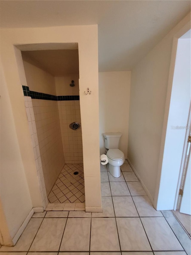 bathroom with toilet, tiled shower, baseboards, and tile patterned flooring