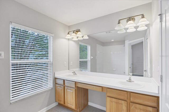 full bath featuring tile patterned floors, baseboards, double vanity, and a shower