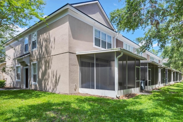 rear view of property with a sunroom, stucco siding, and a lawn