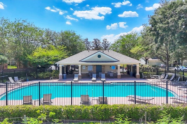 community pool with fence, a patio, and view of wooded area