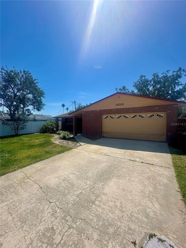ranch-style home featuring concrete driveway, fence, an attached garage, a front lawn, and brick siding