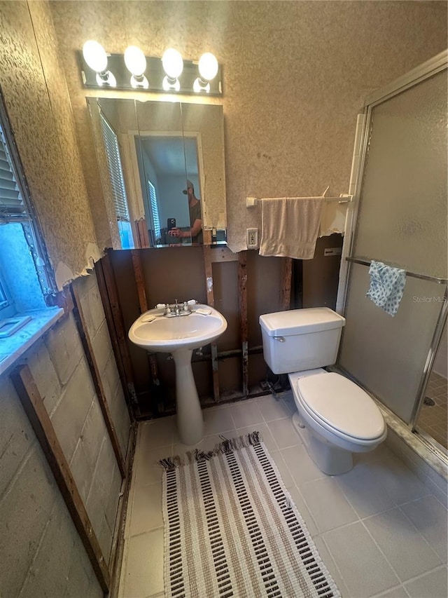 bathroom featuring toilet, wallpapered walls, a sink, a stall shower, and tile patterned flooring