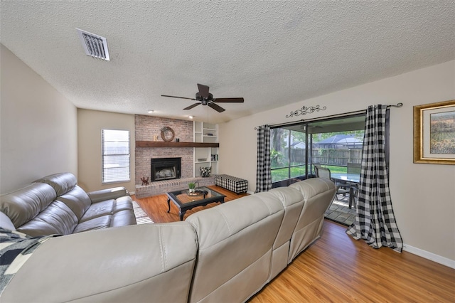 living area with a textured ceiling, light wood finished floors, visible vents, a ceiling fan, and a fireplace