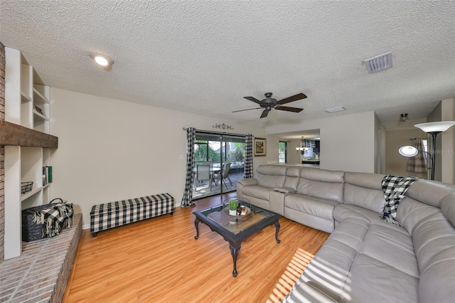living area with a ceiling fan, a textured ceiling, light wood-style floors, and visible vents