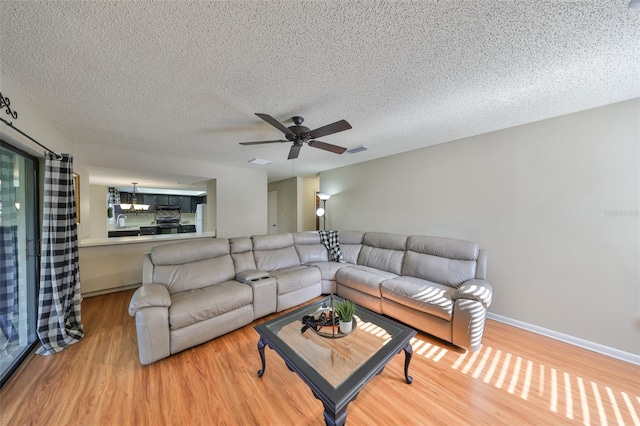 living area featuring baseboards, a textured ceiling, visible vents, ceiling fan, and wood finished floors