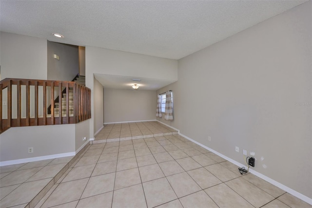 empty room with baseboards, stairs, a textured ceiling, and tile patterned flooring