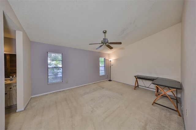 empty room featuring a textured ceiling, baseboards, ceiling fan, light carpet, and lofted ceiling