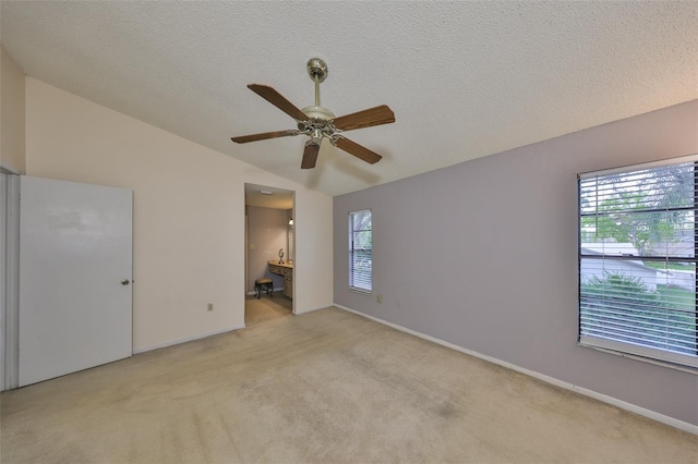 unfurnished bedroom with light carpet, a textured ceiling, lofted ceiling, ensuite bath, and baseboards