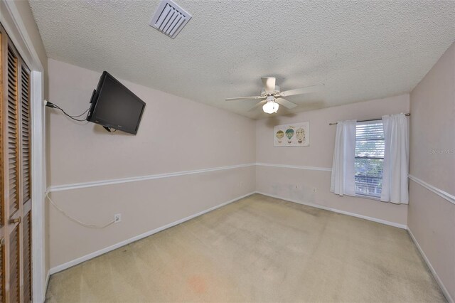 unfurnished room featuring carpet flooring, baseboards, a textured ceiling, visible vents, and a ceiling fan