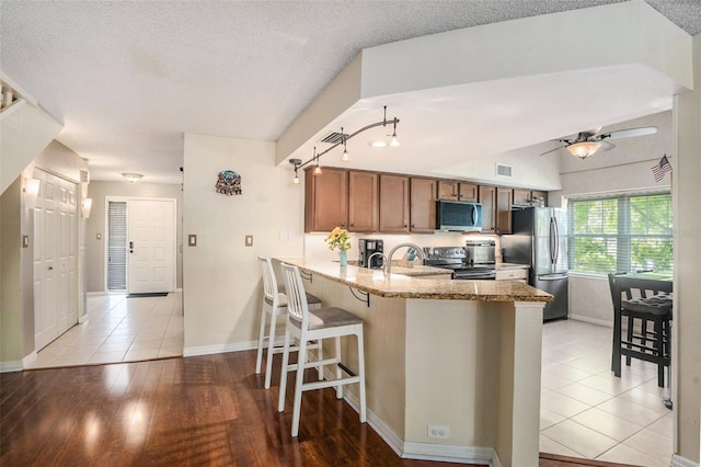 kitchen with stainless steel appliances, a peninsula, baseboards, and brown cabinetry