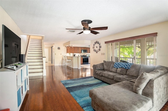 living room with dark wood-style floors, a textured ceiling, visible vents, stairs, and ceiling fan