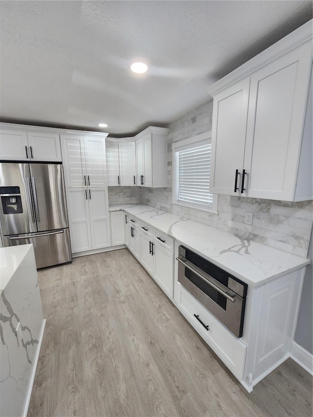 4619 Helena St NE, Saint Petersburg, FL 33703 - kitchen with white cabinets, tasteful backsplash, appliances with stainless steel finishes, and light wood finished floors