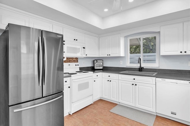 kitchen featuring dark countertops, a sink, white appliances, light wood-style floors, and white cabinetry