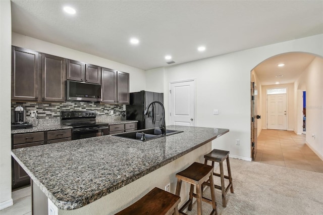 6882 Silverado Ranch Blvd, Zephyrhills, FL 33541 - kitchen with an island with sink, a breakfast bar, a sink, arched walkways, and black appliances