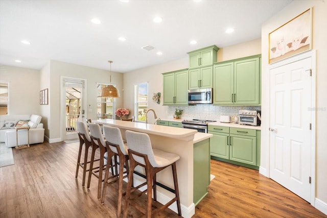 kitchen with a kitchen island with sink, light countertops, green cabinetry, light wood finished floors, and appliances with stainless steel finishes